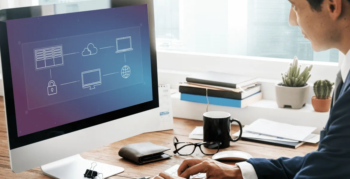 Man working at a desk with a computer displaying a cloud network diagram.